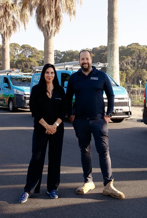 William and Emily, directors of Proximity Plumbing, standing in front of the van fleet